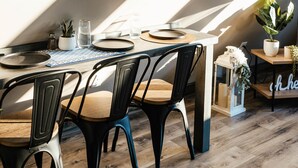 Comedor con techo alto y tragaluces, con una mesa dispuesta para dos personas, sillas, una planta pequeña y un objeto decorativo sobre la mesa.