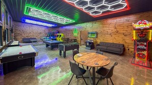 Una habitación con mesa de billar, mesa de futbolín y una mesa con sillas.