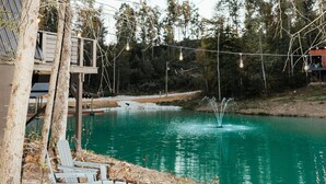 Un espacio al aire libre junto al lago con sillas tipo Adirondack, una hoguera y una terraza de madera con vistas a un lago color turquesa.
