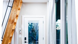 Un salon moderne avec des canapés en cuir, un escalier en bois et une vue sur une forêt, visible à travers une porte vitrée.