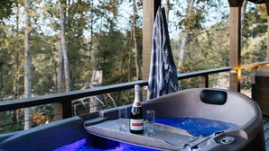 Un bain à remous avec une bouteille de champagne Ballatore et deux verres, installé sur un balcon offrant une vue sur les arbres.