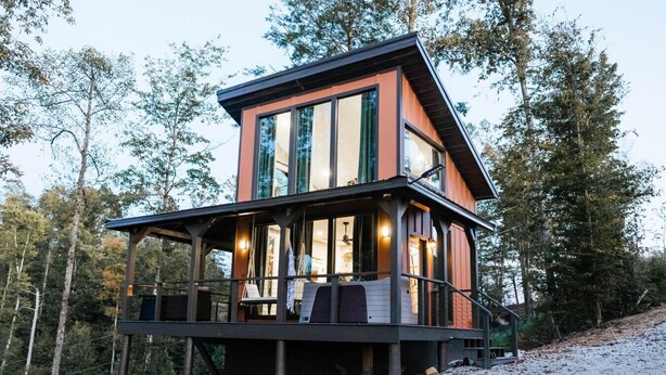 Une cabane moderne dotée d’un balcon, de grandes fenêtres et d’une terrasse.