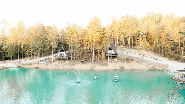 Una cabaña junto al lago con un muelle, rodeada de árboles y un lago turquesa cristalino.