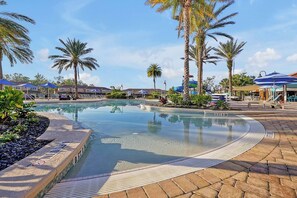 A swimming pool with a clear water edge, surrounded by palm trees and lounge chairs.