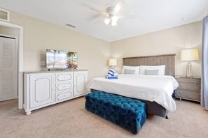 A hotel room with a bed, a TV on a dresser, a ceiling fan, and a bench.