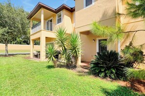 A two-story building with a balcony, surrounded by well-maintained grass and various tropical plants.