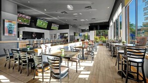 Ein geräumiges Restaurant mit mehreren Tischen und Stühlen, großen Fenstern und einer hohen Decke mit eingelassener Beleuchtung.