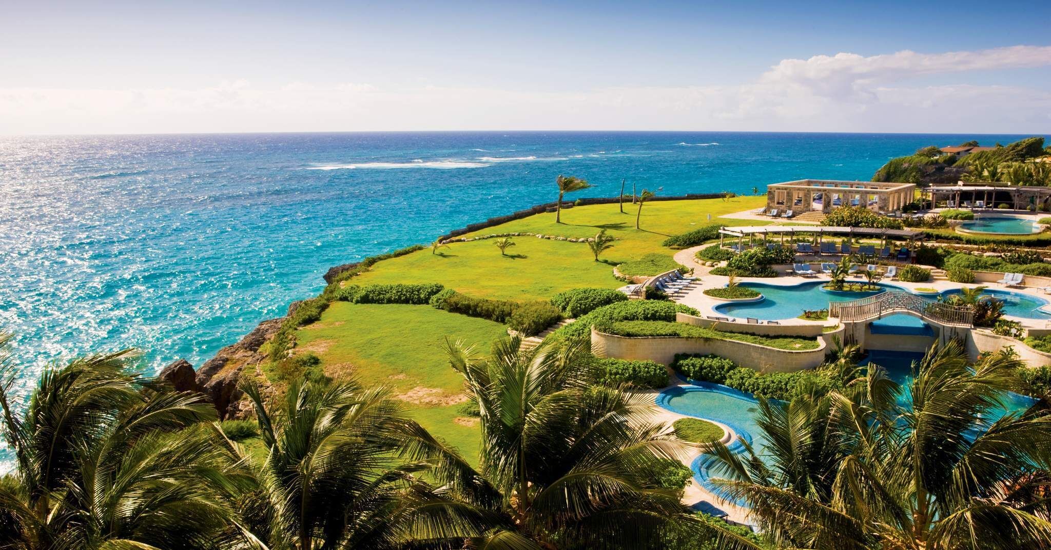 A resort with multiple swimming pools, a large lawn, and a view of the ocean.
