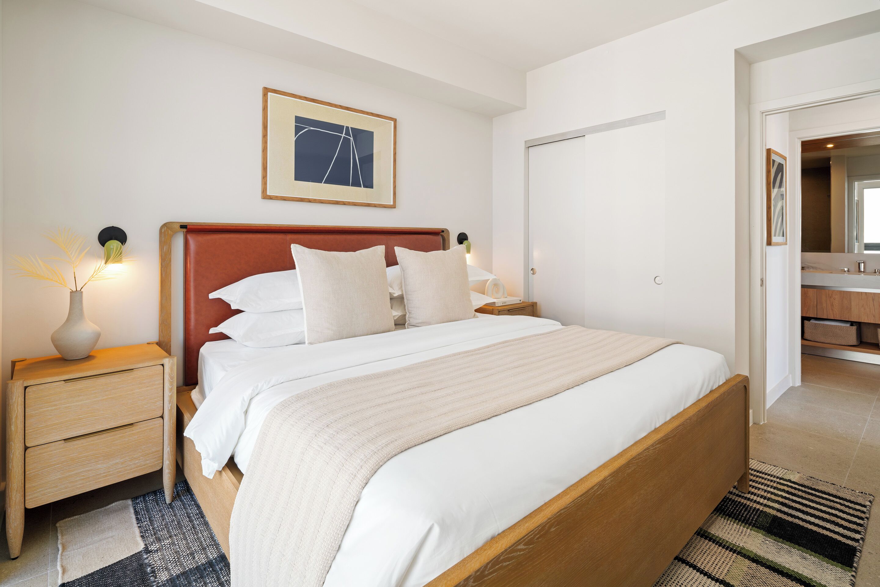 A neatly made bed with a wooden headboard, a bedside table with a lamp, and a framed picture on the wall.