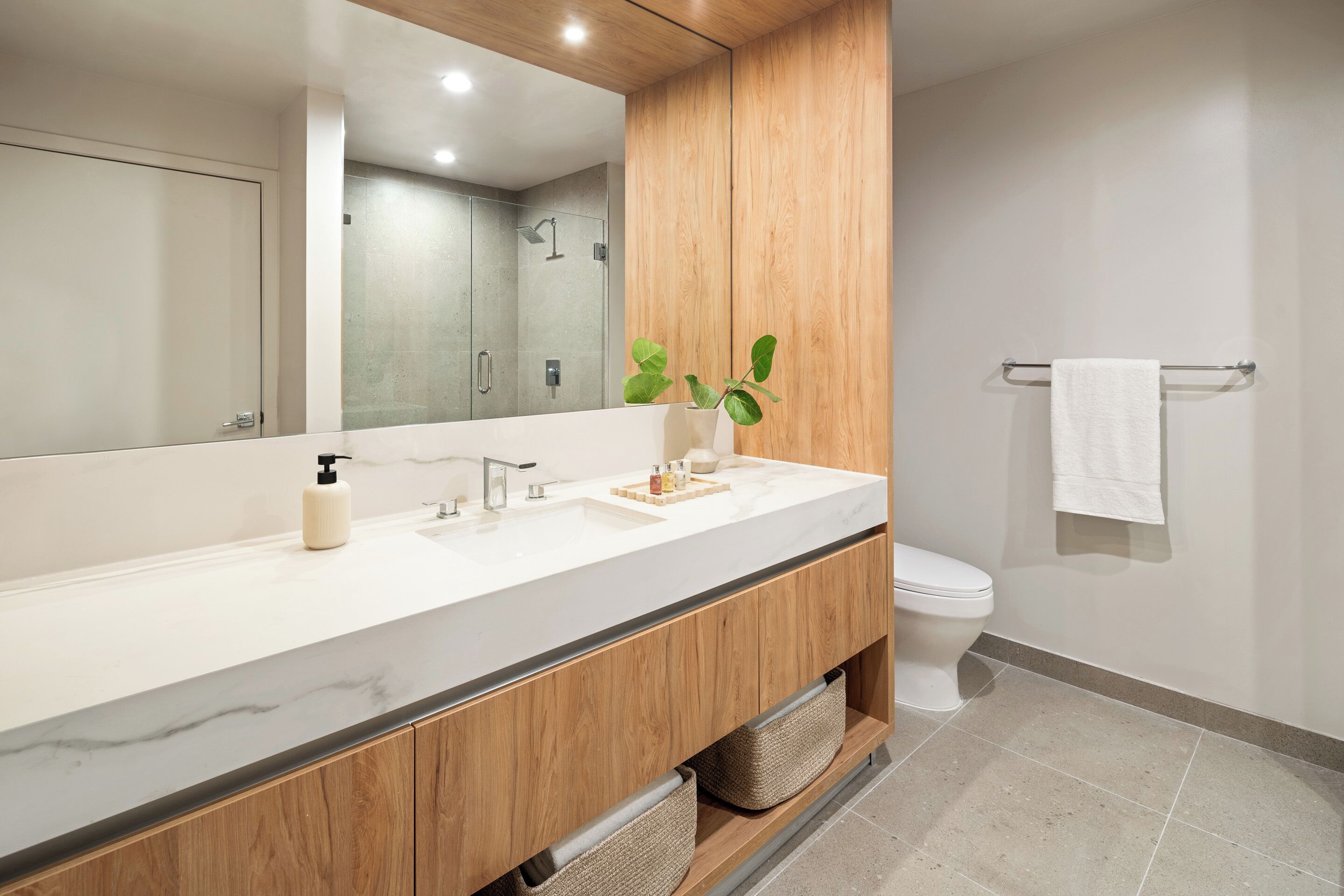 A modern bathroom with a wooden vanity, a large mirror, a white sink, and a toilet.