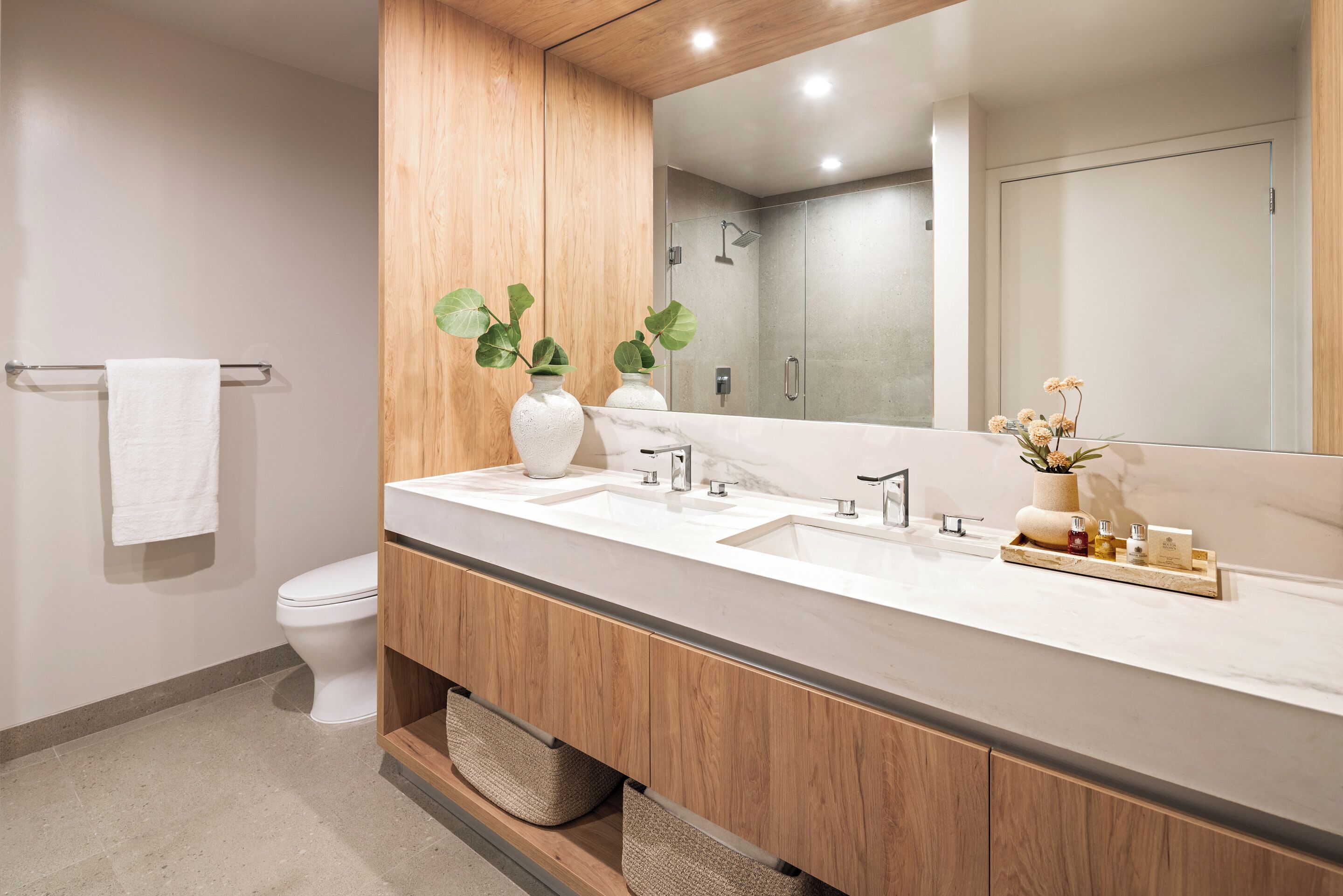 Une salle de bain moderne avec un meuble-lavabo en bois, deux vasques, des toilettes et un grand miroir.