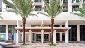 Ein moderner Hotel Eingang mit Palmen, einem Schild mit der Aufschrift "THE CROSBY" und einem Schachbrettmuster-belagten Gehweg.