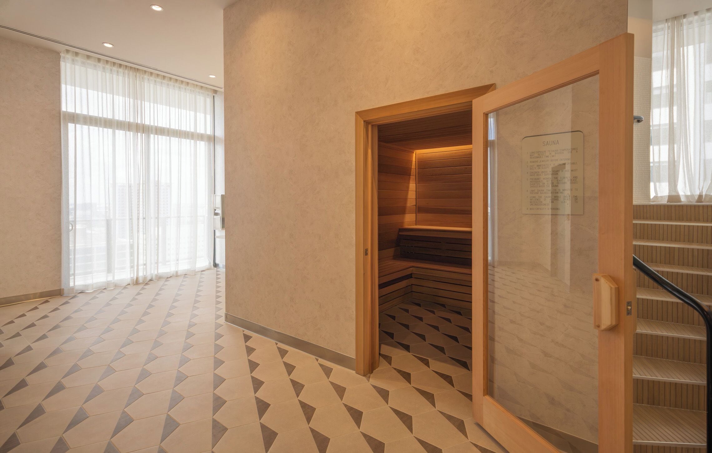 Un intérieur moderne avec un sol à motifs géométriques, un sauna doté de bancs en bois et un escalier avec une porte en verre.