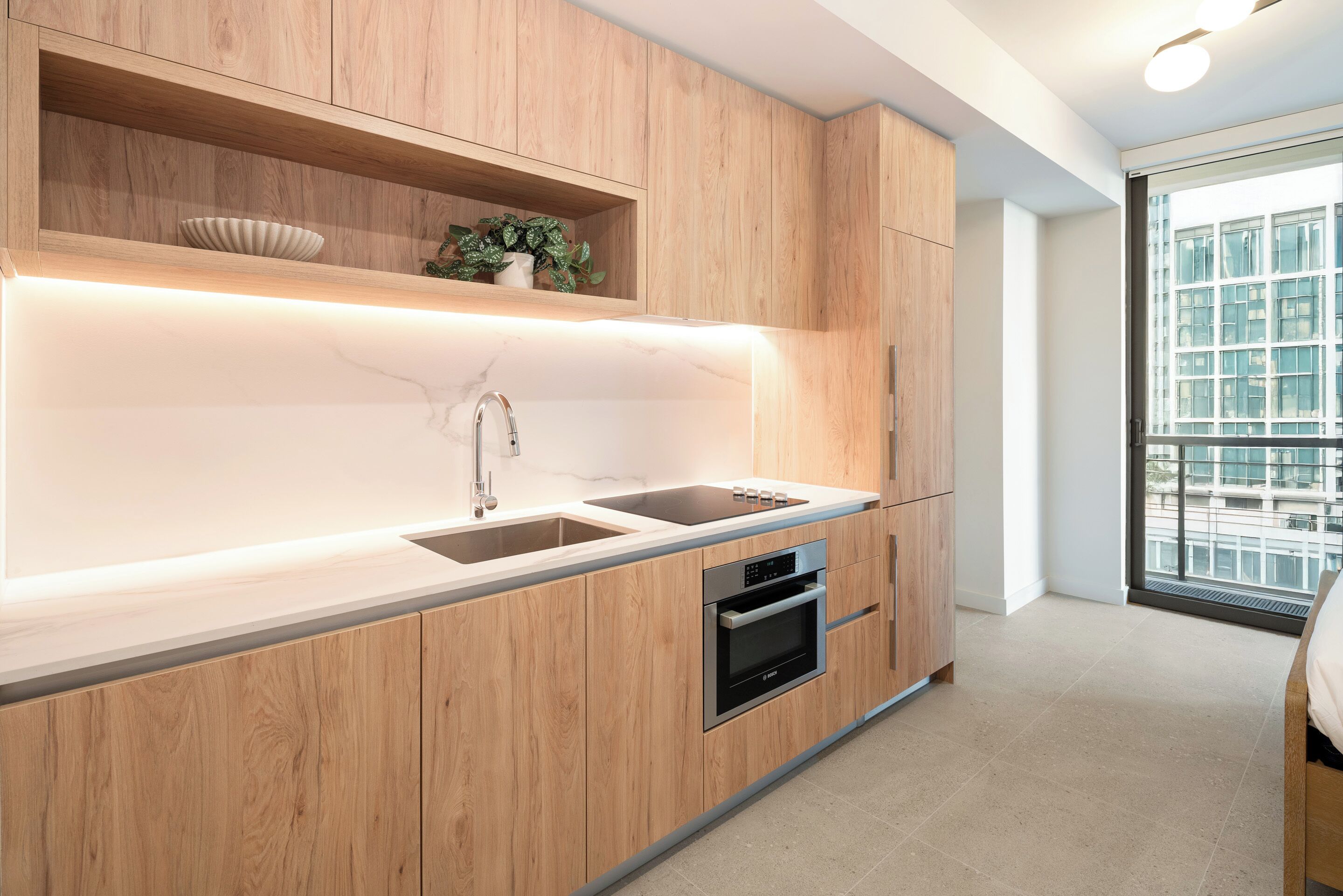 A modern kitchen with wooden cabinets, a built-in oven, and a large window offering a view of the city.