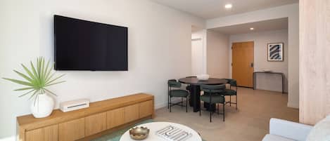 A modern living room with a flat-screen TV, a wooden console table, a round coffee table, and a dining area with a round table and chairs.
