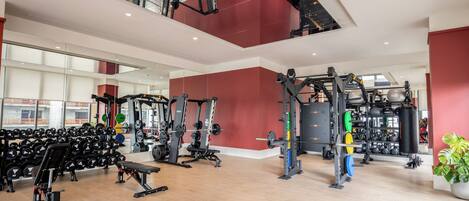 A modern gym with various weightlifting equipment, mirrors, and a large mirror on the ceiling.