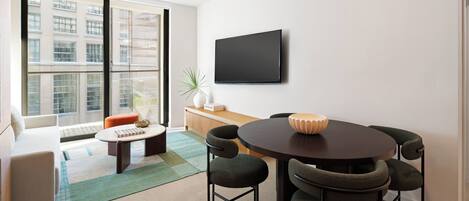 Un salon moderne avec une table ronde, quatre chaises, un canapé, une table basse et un téléviseur à écran plat fixé au mur.