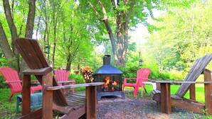 En rustik utomhusplats med sittmöbler, inklusive Adirondack-stolar, och en vedeldad kamin.