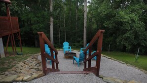 Una terraza de madera con sillas Adirondack y un hogar para fuego, rodeada por un camino de grava y un borde de piedra.