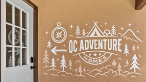 Eine Wand mit Kompass, Zelt, Bäumen und Bergen, beschriftet mit "OC ADVENTURE HOMES".