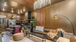 Una sala moderna con sofá, reposapiés y una mesa de centro. Hay una zona de cocina con barra y taburetes.