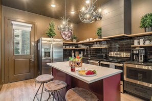 Een moderne keuken met een centraal eiland, roestvrijstalen apparatuur en decoratieve verlichting.