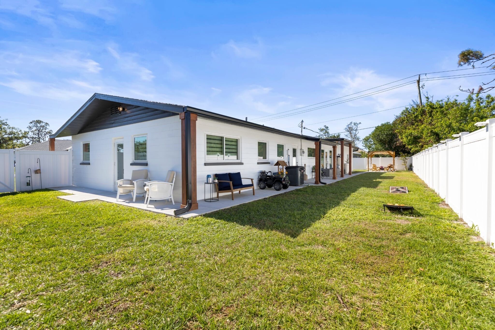 Ein modernes eingeschossiges Haus mit überdachter Terrasse, Rasenfläche und weißem Zaun.