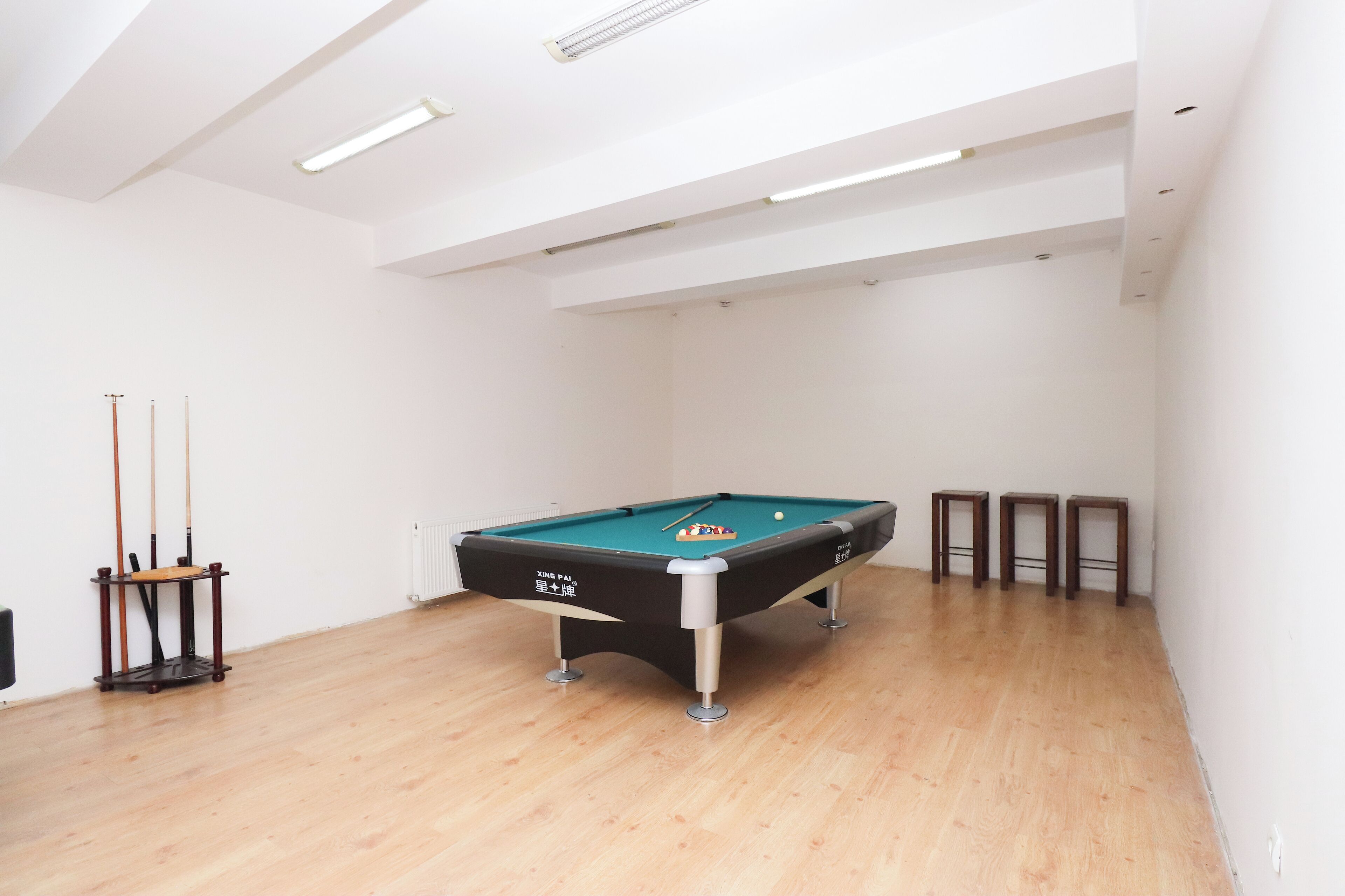 Une table de billard dans une pièce dont le sol est en bois et les murs sont blancs.