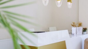 Un mostrador de recepción con encimera blanca, tres candelabros de cristal colgantes y una planta con plumas de pluma pampa seca.