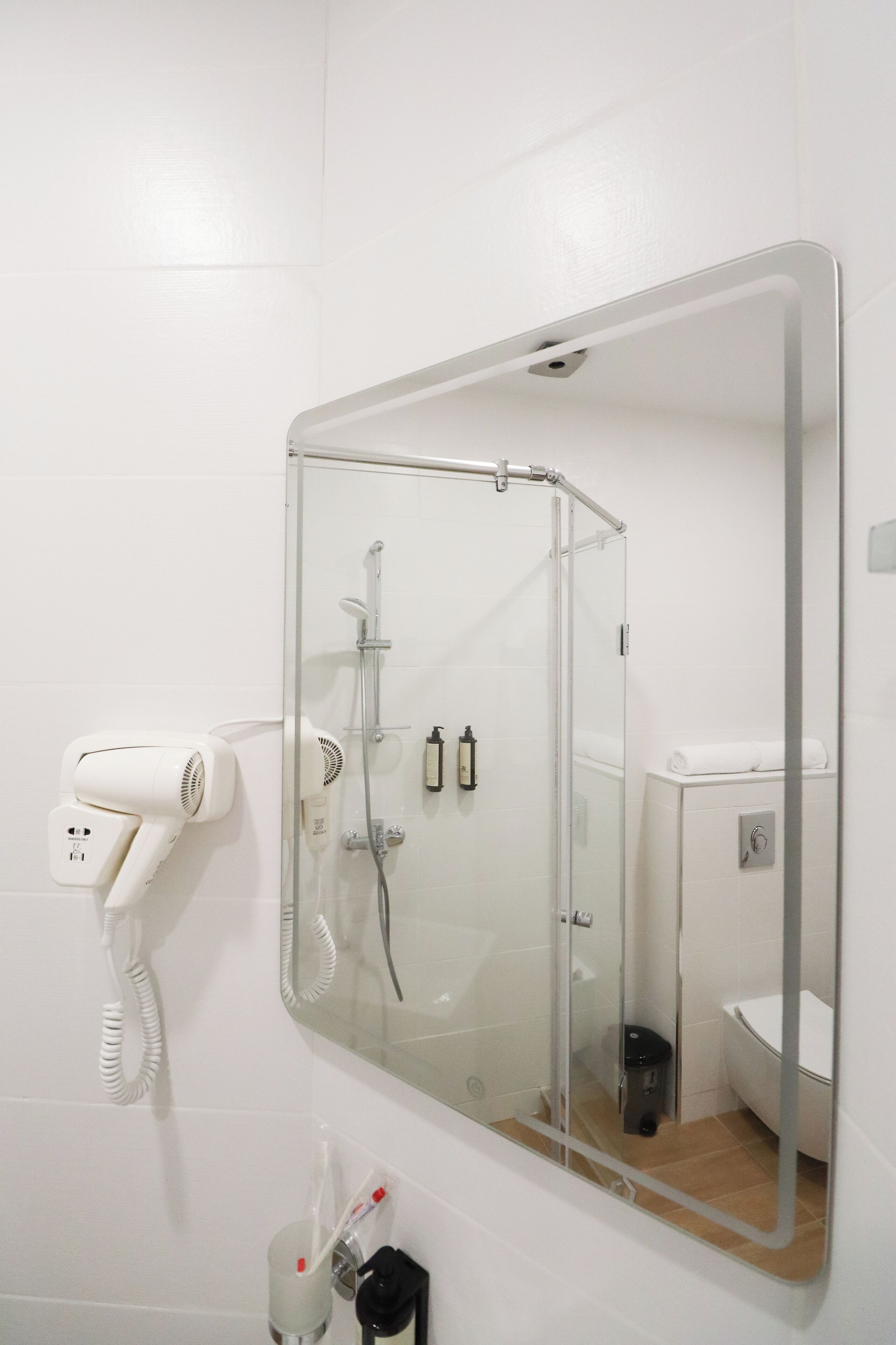 A bathroom with a glass-enclosed shower, a white toilet, and a hairdryer on a wall-mounted stand.