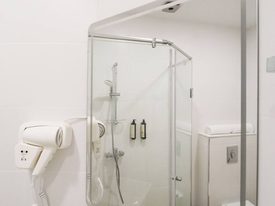 A bathroom with a glass-enclosed shower, a white toilet, and a hairdryer on a wall-mounted stand.