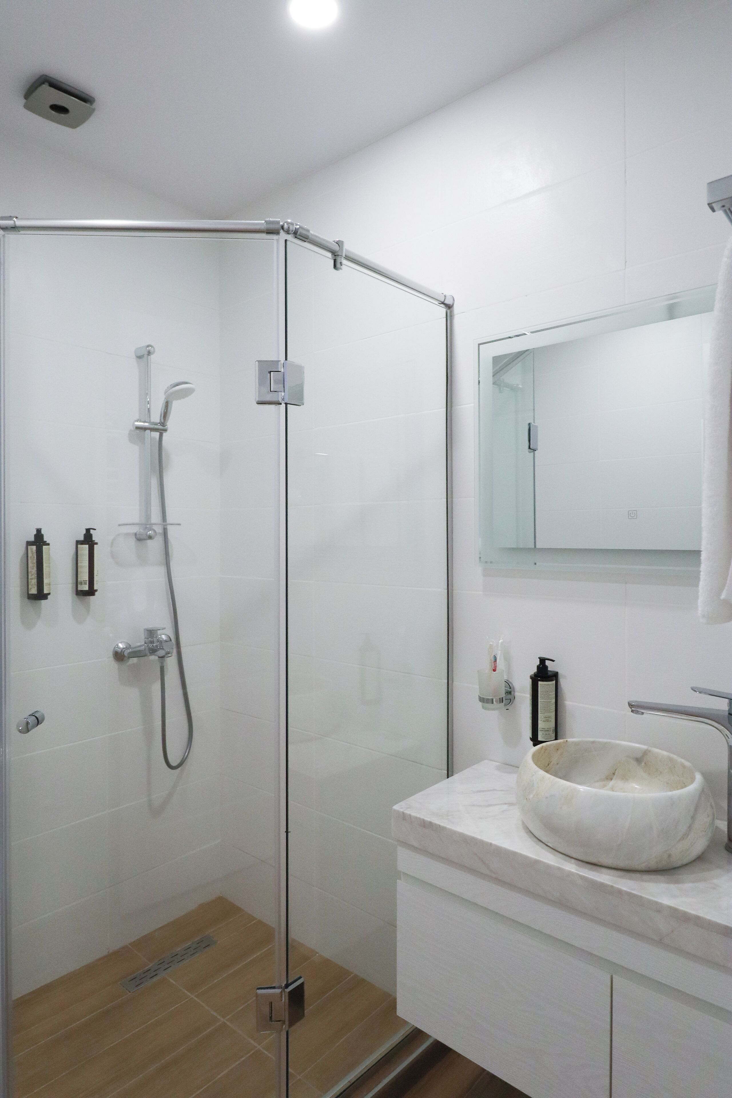 A modern bathroom with a glass-enclosed shower, a marble sink, and a large mirror.