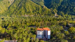 Un edificio de varios pisos con techo rojo, rodeado de un bosque denso y montañas.