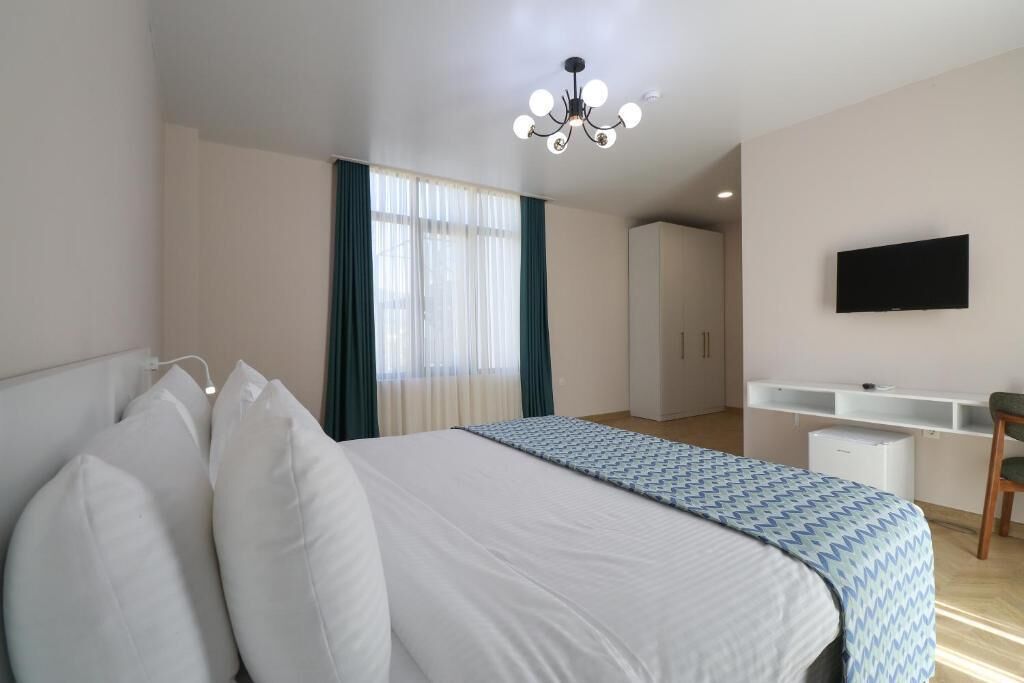 Una habitación de hotel con una cama grande, un escritorio con silla, un televisor montado en la pared y un armario.