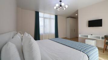 Una habitación de hotel con una cama grande, un escritorio con silla, un televisor montado en la pared y un armario.