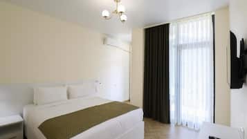 Habitación de hotel con cama, mesita de noche, televisor montado en la pared y ventana con cortinas.