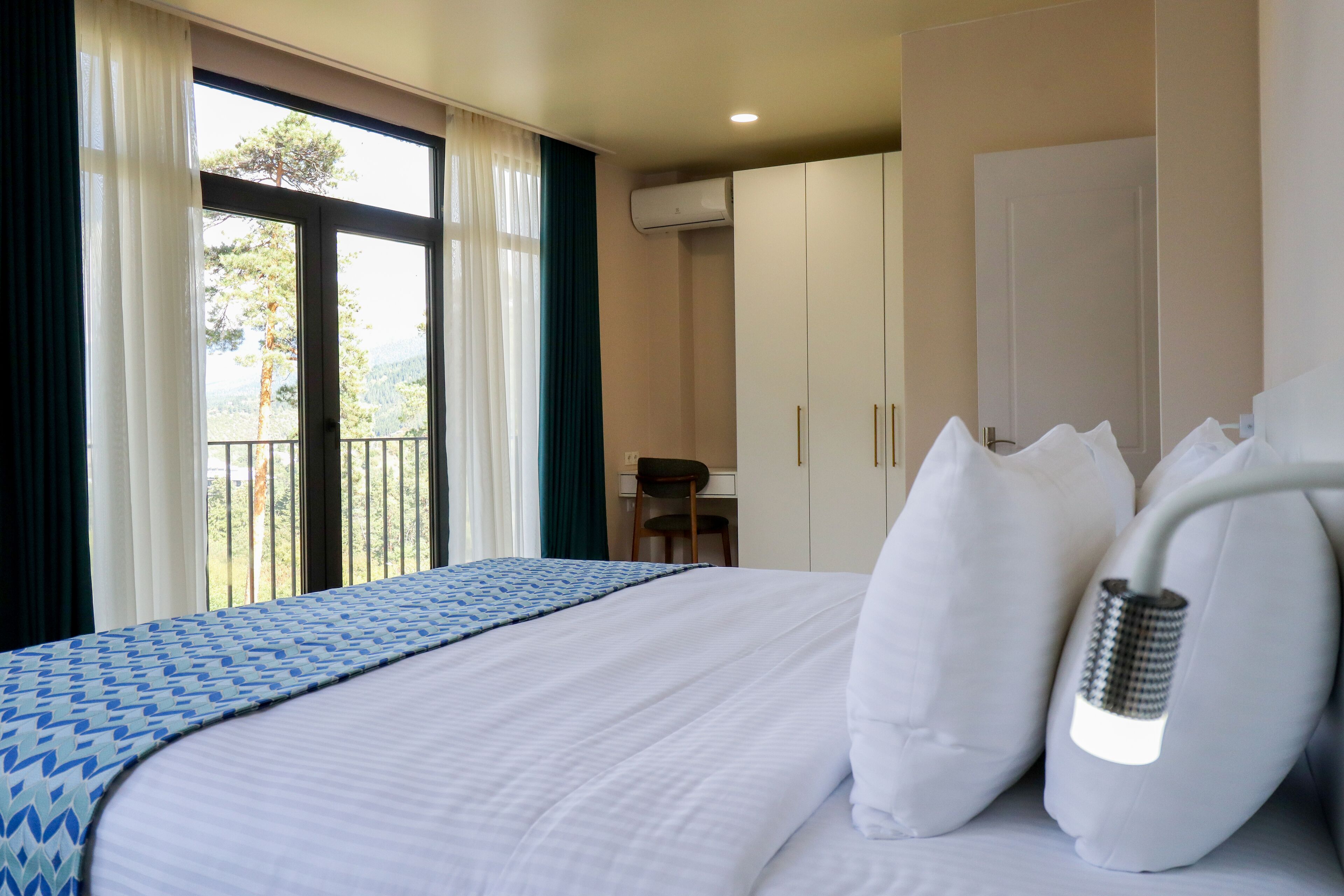 Habitación de hotel con cama, escritorio y vistas a árboles por la ventana.