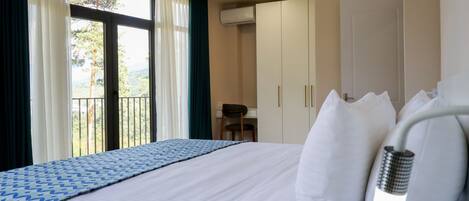 Habitación de hotel con cama, escritorio y vistas a árboles por la ventana.