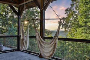 A hammock on a wooden deck with a view of a forest and mountains.