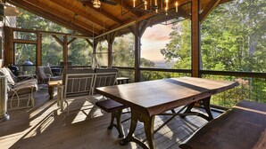 A covered outdoor area with a wooden table and benches, a ceiling fan, and a view of trees. - Pop`s Peak| Morganton, GA (Morganton)