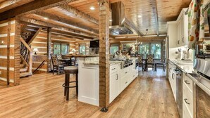 A log cabin interior with a central island kitchen, wooden beams, and a staircase. - Pop`s Peak| Morganton, GA (Morganton)