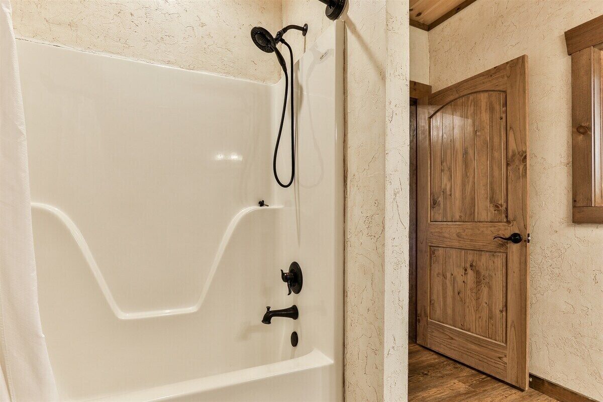 A white bathtub with a showerhead and controls, a wooden door, and a textured wall.