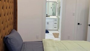 Ein Schlafzimmer mit einer gepolsterten Kopfstütze, einem Bett mit grau-gelber Bettwäsche und einem weißen Kleiderschrank im Hintergrund.