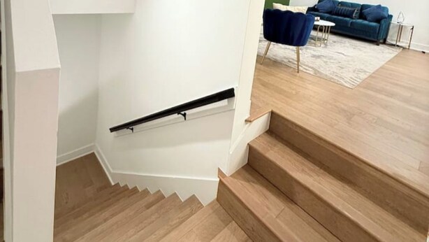 Eine Treppe mit Holzboden und einem schwarzen Geländer, das zu einer Zwischenebene führt.