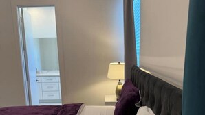 Een slaapkamer met een bed, een nachtkastje met een lamp en een deur naar een badkamer.