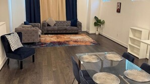 Een moderne woonkamer met een grijze bank, een eettafel met placemats en een donkerblauwe fauteuil.