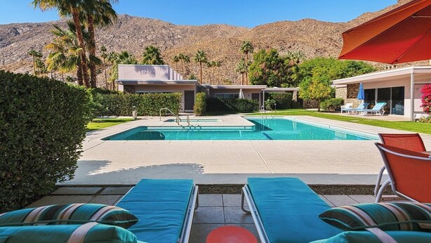A pool area with lounge chairs, a pool, and a mountain backdrop. - 2-bedroom condo in Historic Tennis Club (Palm Springs)