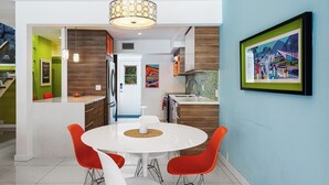 A modern kitchen with a round dining table and red chairs, a hanging light fixture, and a framed picture on the wall. - 2-bedroom condo in Historic Tennis Club (Palm Springs)
