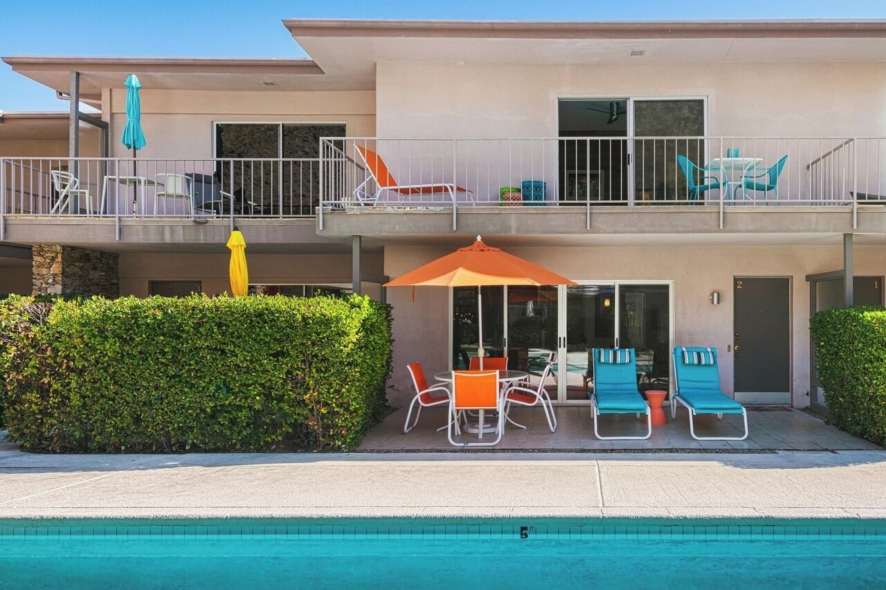 A two-story building with a pool, outdoor seating, and a balcony with lounge chairs.