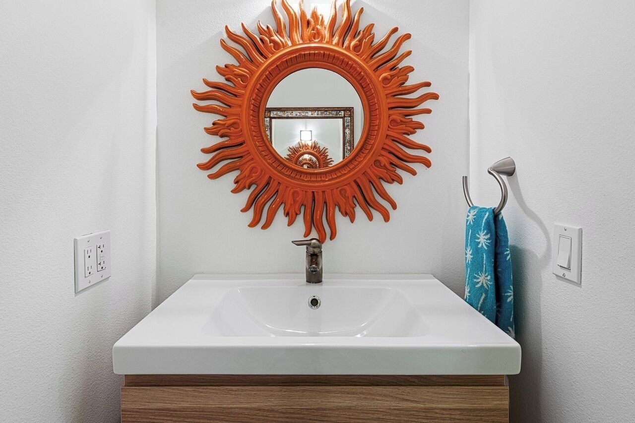 Un baño con un lavamanos blanco, un espejo con diseño de sol y un toallero con una toalla azul.